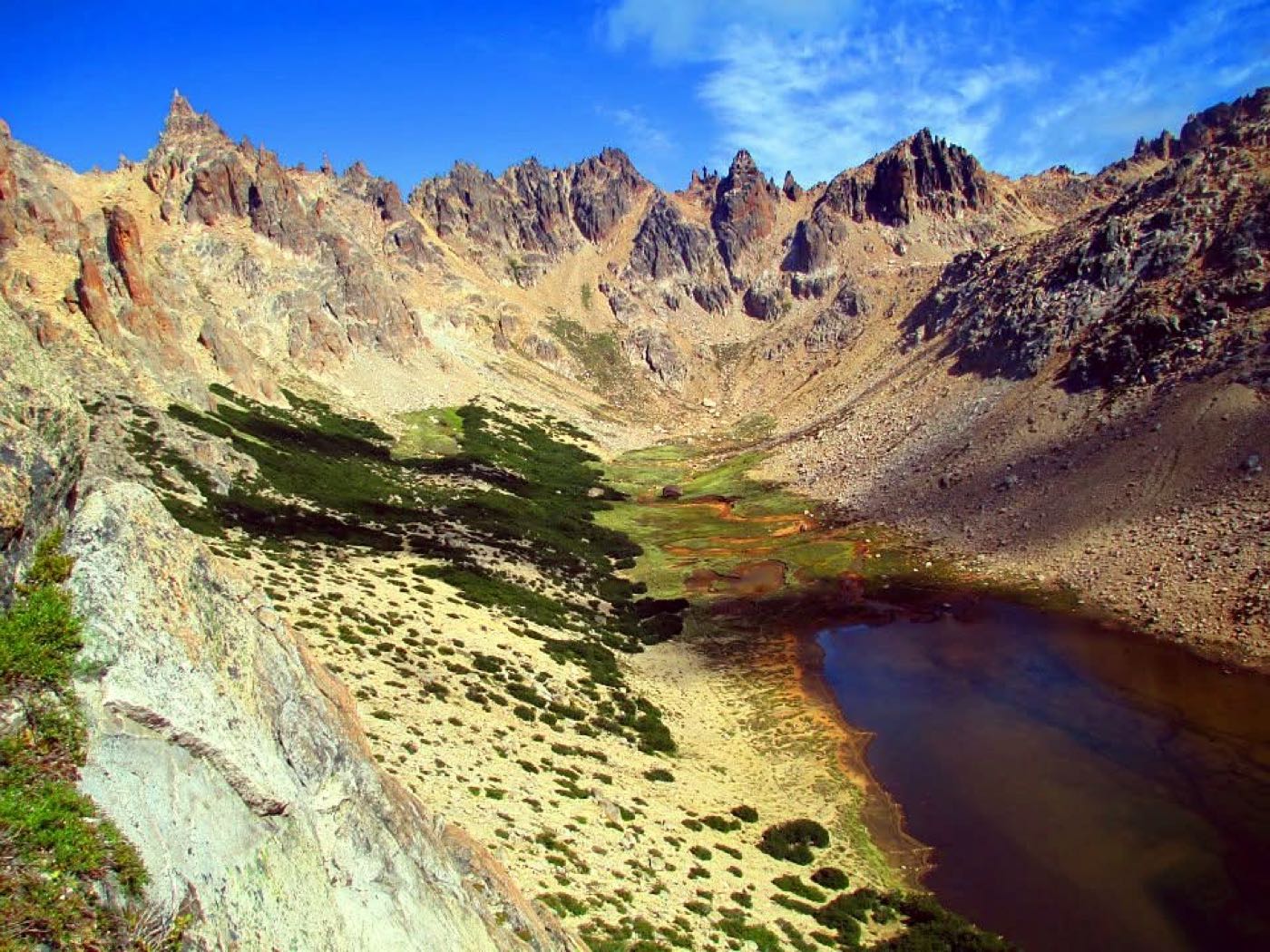 A green alpine valley and dark lagoon beneath jagged granite peaks