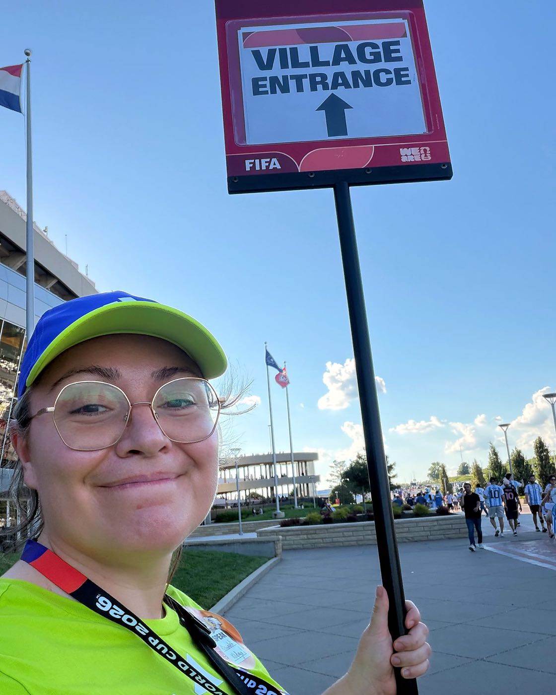 Emily in her volunteer uniform holding a Village Entrance sign outside Arrowhead Stadium